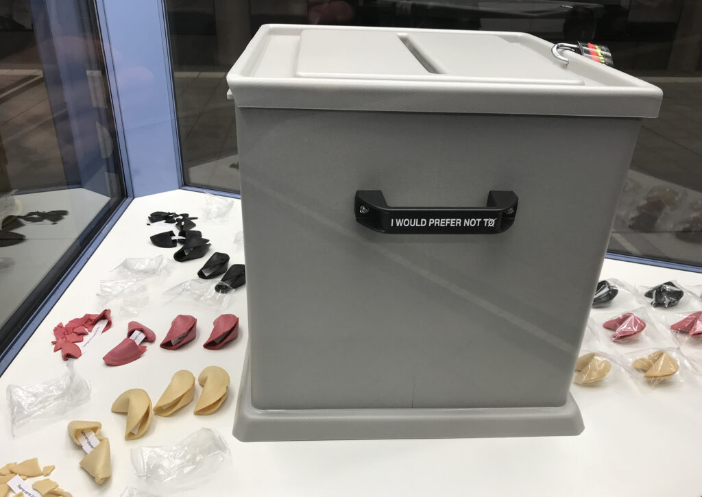 Ansicht Halbtotale - Wahlurne mit aufgereihten schwarz rot gold Glückskeksen in Vitrine - Kunstinstallation - I would prefer not to (X) - präsentiert von Warte Positionen, U-Bahnsteig Bockenheimer Warte