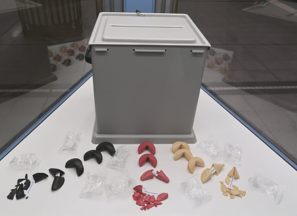 Ansicht Halbtotale - Wahlurne rückseitig mit aufgebrochenen schwarz rot gold Glückskeksen in Vitrine - Kunstinstallation - I would prefer not to (X) - präsentiert von Warte Positionen, U-Bahnsteig Bockenheimer Warte