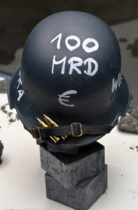 Ansicht Nah - Helm mit Aufschrift 100 Milliarden Euro, auf Steinen platziert - Kunstinstallation - Krisen-Narrative - präsentiert von Warte Positionen, U-Bahnsteig Bockenheimer Wart