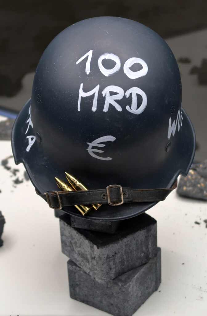 Ansicht Nah - Helm mit Aufschrift 100 Milliarden Euro, auf Steinen platziert - Kunstinstallation - Krisen-Narrative - präsentiert von Warte Positionen, U-Bahnsteig Bockenheimer Wart