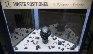 Ansicht Totale - Helm mit Aufschrift Bazooka, auf Steinen platziert, Los auf Stein geschrieben - Kunstinstallation - Krisen-Narrative - präsentiert von Warte Positionen, U-Bahnsteig Bockenheimer Wart